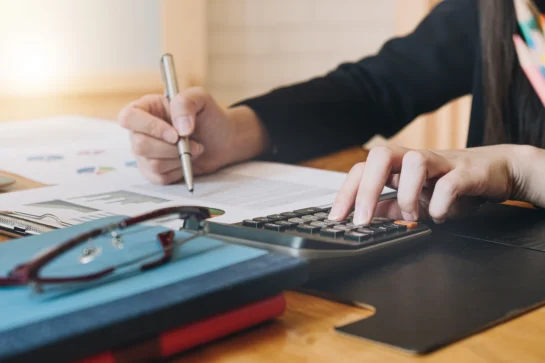 Pessoa calculando dados financeiros com calculadora e gráficos em papel sobre a mesa. Ela está procurando o que é CAC e sua importância.