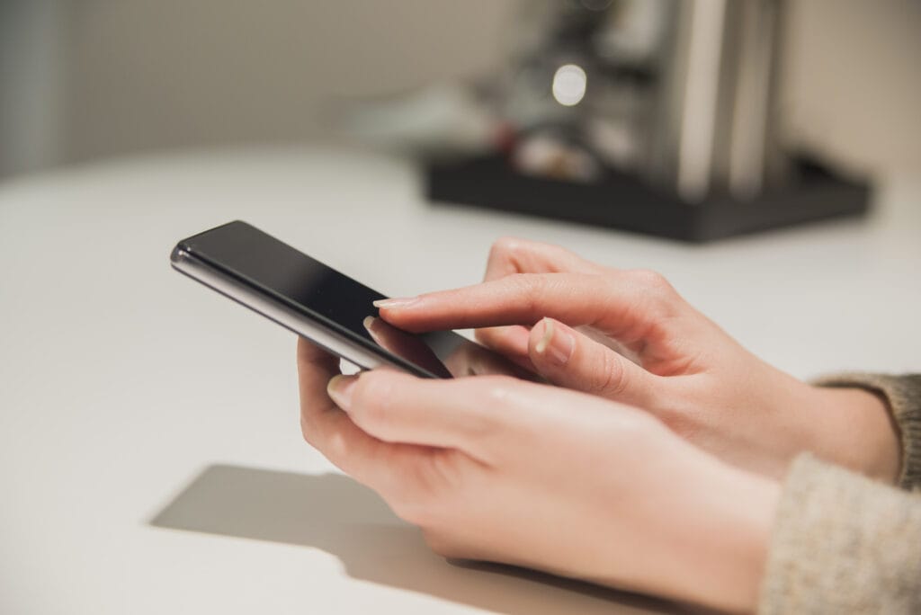 A imagem mostra as mão de uma cliente segurando um celular. Ela está efetuando um pagamento após receber uma mensagem de cobrança por sms.