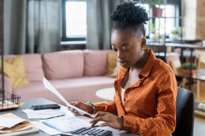 Mulher negra revisando documentos e usando calculadora, ilustrando a gestão de diferentes tipos de boleto bancário.