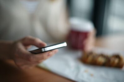 Pessoa verifica lembrete de pagamento no smartphone. Ao fundo há uma mesa de cozinha desfocada.