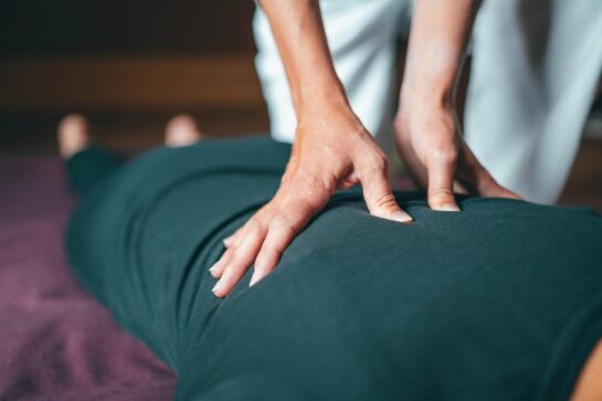 Na imagem temos uma massagista fazendo massagem em um cliente. Ele está deitado de costas e a moça está em pé um as mãos sobre as suas costas. A imagem busca representar marketing para massagens.