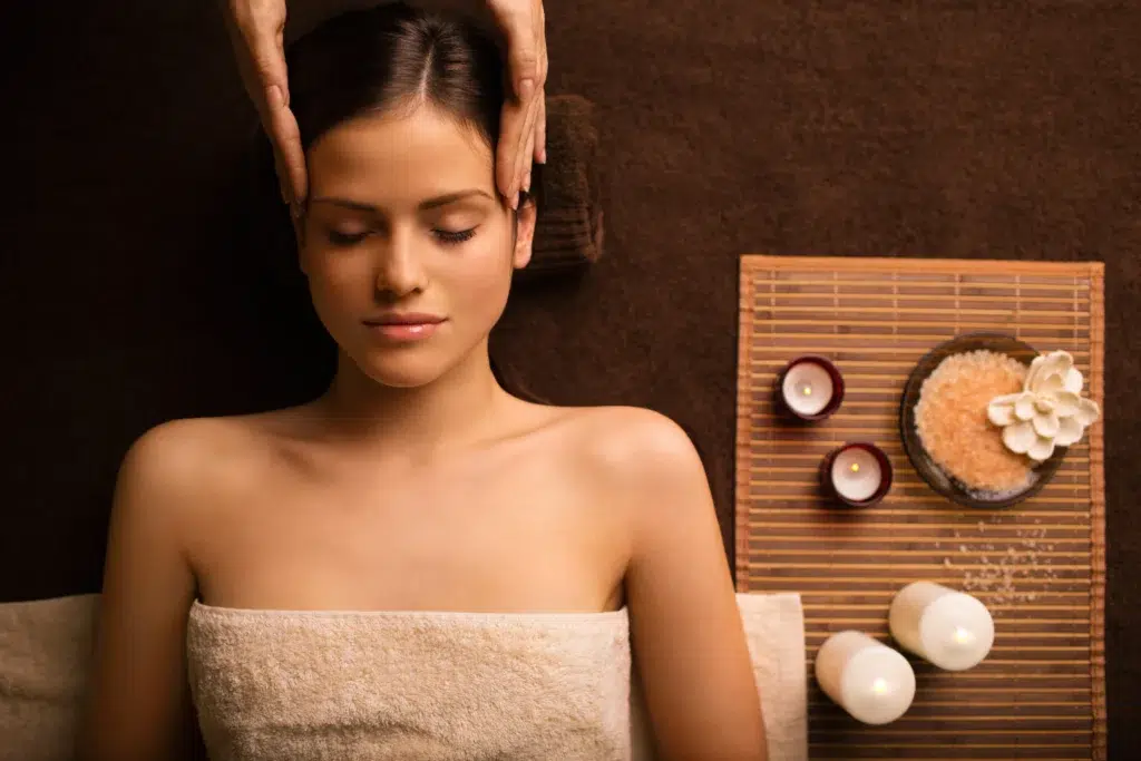 Mulher relaxando durante uma massagem com velas e itens de spa. É uma imagem utilizada em marketing para massagens.