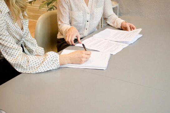 Temos duas mulheres sentadas em volta de uma mesa conversando. Elas estão pesquisando sobre como conseguir crédito empresarial.