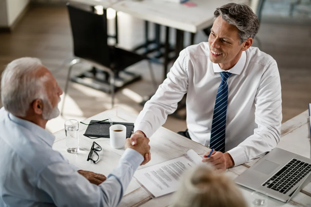 Dois homens apertam as mãos em um escritório após assinarem um contrato de empréstimo empresarial.