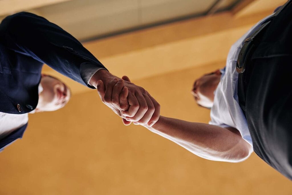 Na imagem, dois homens, um de frente para o outro, apertando as mãos. A imagem representa como negociar com fornecedores.