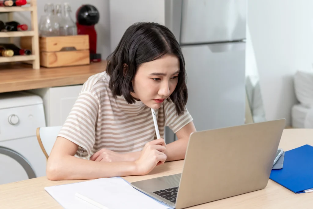 Mulher empreendedora sentada em frente ao computador. Está pesquisando o melhor banco para emitir boletos.