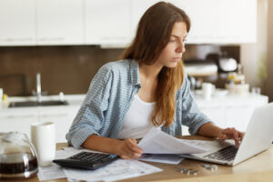 Na imagem, temos uma mulher com seu computador sobre a mesa. Ela esta pesquisando como emitir nota fiscal mei df.