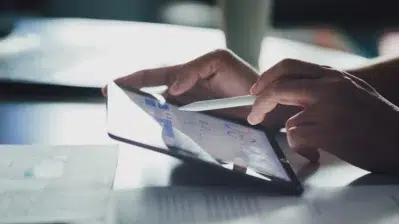 Homem usando tablet, segurando caneta e analisando gráficos, enquanto realiza o controle de fluxo de caixa.