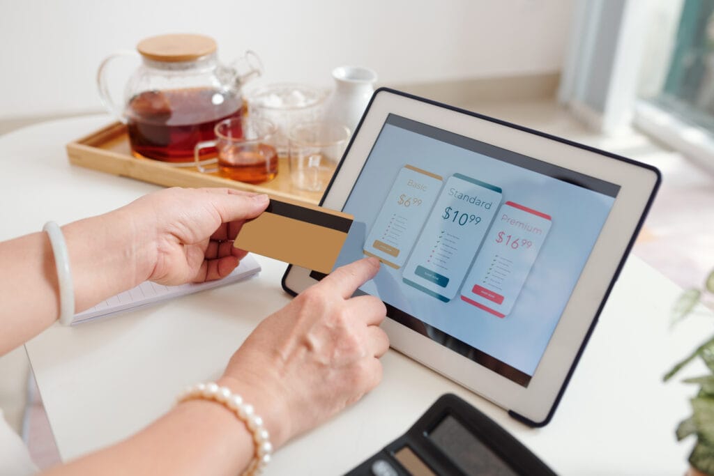 A imagem mostra uma pessoa segurando um tablet e um cartão. Na tela está o checkout onde ela está fazendo o pagamento recorrente.