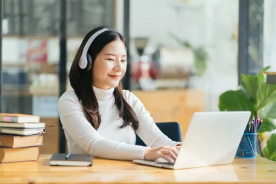 Mulher sorrindo usando fones de ouvido e trabalhando em um laptop, utilizando sistema de cobrança automatizado.