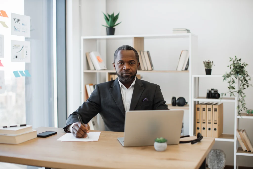 Homem de terno sentado à mesa com laptop, exemplificando características de um administrador.