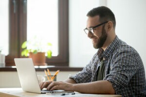 A imagem mostra um empreendedor em seu escritório, mexendo em seu computador. Ele está feliz pois encontrou o melhor software de cobrança para sua empresa.