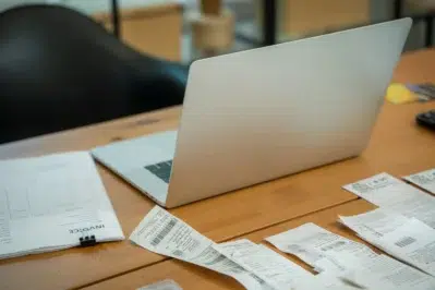 Pessoa organizando contas com notebook e faturas na mesa, em contexto de escritório, ilustrando como emitir boleto com praticidade.