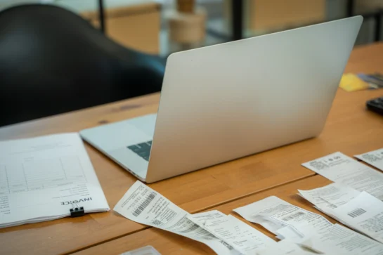 Pessoa organizando contas com notebook e faturas na mesa, em contexto de escritório, ilustrando como emitir boleto com praticidade.