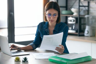 a imagem tem uma mulher, ela está apontando para um notebook que está encima da mesa. A imagem busca representar Como emitir boleto de cobrança.