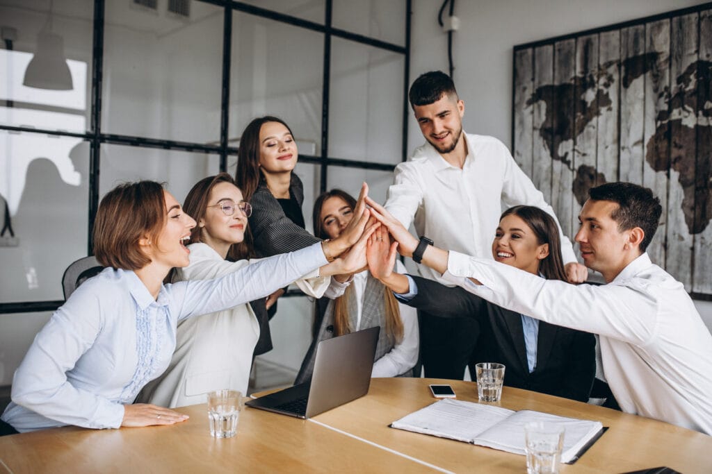 A imagem mostra a equipe de vendas reunida, com as mãos ao centro. Todos estão feliz após entender estratégias de como fidelizar clientes.