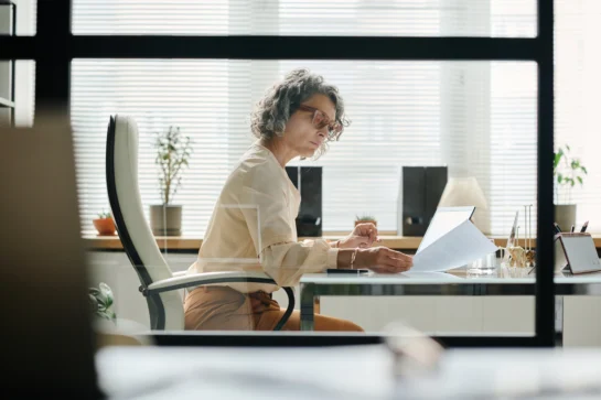 Mulher lendo a respeito da Lei da Duplicata, sentada em seu escritório.