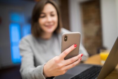 Mulher está segurando um telefone celular em uma das mãos. Ela está fazendo uma cobrança por link de pagamento.