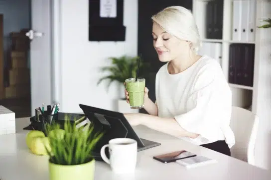 Mulher em casa, usando tablet e tomando suco verde, representando que Pessoa Física pode emitir boleto facilmente.