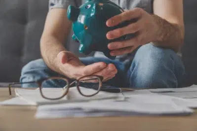 Pessoa segurando um cofrinho verde enquanto analisa documentos financeiros, refletindo sobre inadimplência financeira.