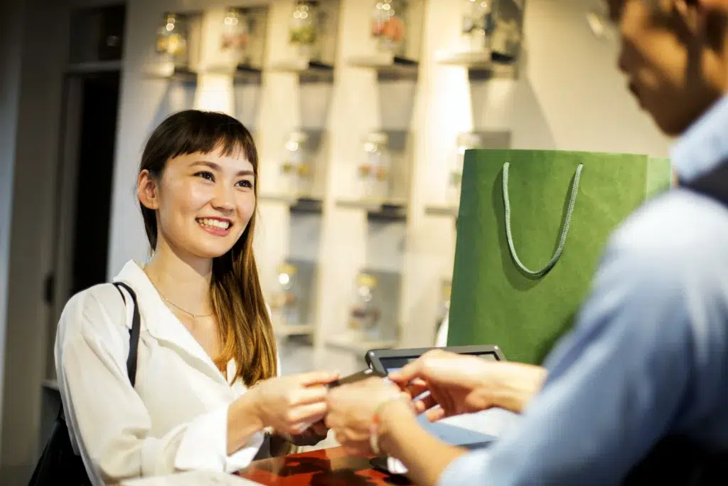 Mulher sorridente realizando pagamento em loja, representando a satisfação do cliente com um bom atendimento.