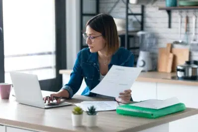 Mulher em um escritório usando laptop e analisando documentos, representando o processo de como emitir DANFE.