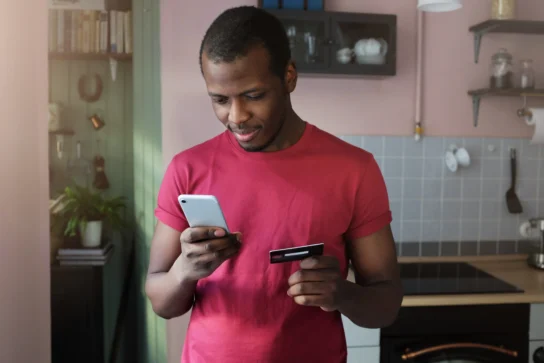 Homem segurando celular e cartão de crédito em mãos. Ele está batalhando pela disputa de chargeback.