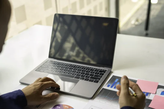 Pessoa mexendo em computador. Do lado direito, analisa gráficos para preparar um e-mail de cobrança para clientes da empresa.