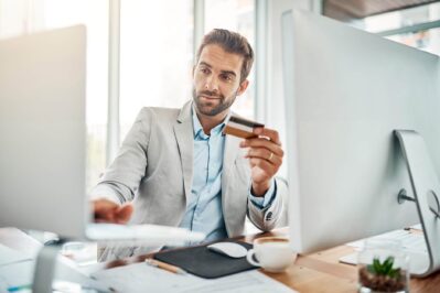 Na imagem, temos um homem em frente do seu computador, com um cartão de crédito na mão, fazendo disputa de chargeback.