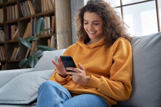 Uma mulher está sentada no sofá mexendo em seu celular. Ela está aprendendo como emitir nota fiscal complementar