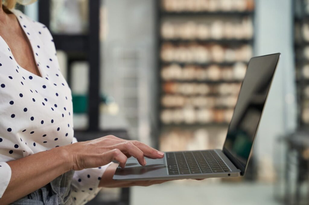 A imagem mostra uma pessoa com as mãos sobre o notebook, o aparelho está sobre a mesa. Na mesa também tem um caderno. A pessoa está buscando emitir nota fiscal eletrônica.
