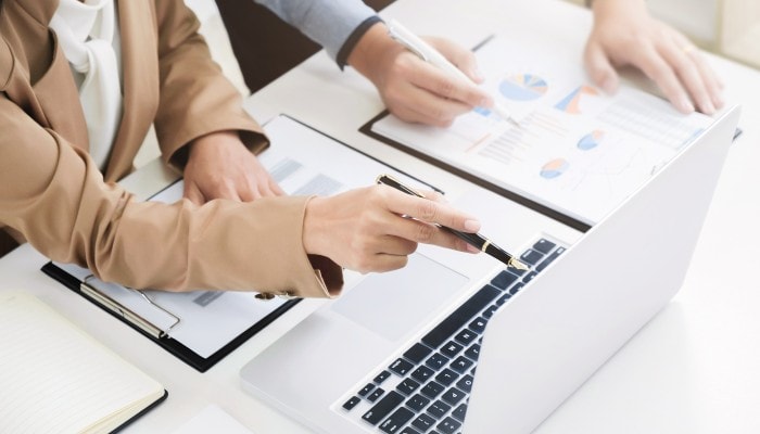 Gestão financeira: tudo o que você precisa saber sobre o assunto 1 Mãos seguram uma caneta enquanto apontam para tela do notebook. Ao lado, estão relatórios financeiros e gráficos de pizza.