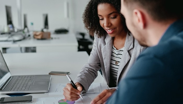Gestão financeira: tudo o que você precisa saber sobre o assunto 4 Empreendedores conversam enquanto olham para relatório financeiro. Ao fundo, há um ambiente de escritório.