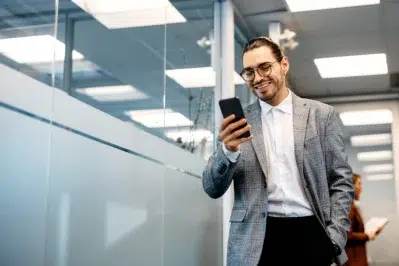 Homem de terno sorrindo e usando smartphone em escritório moderno, representando praticidade do Pix para empresas.