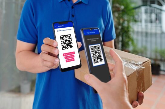 Cliente escaneando QR code do Asaas com o celular. Representante do estabelecimento veste camiseta azul e está em pé segurando o celular com o QR code.