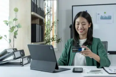 Empresária olhando seu cartão de crédito enquanto tenta abrir conta empresarial em tablet em sua frente.