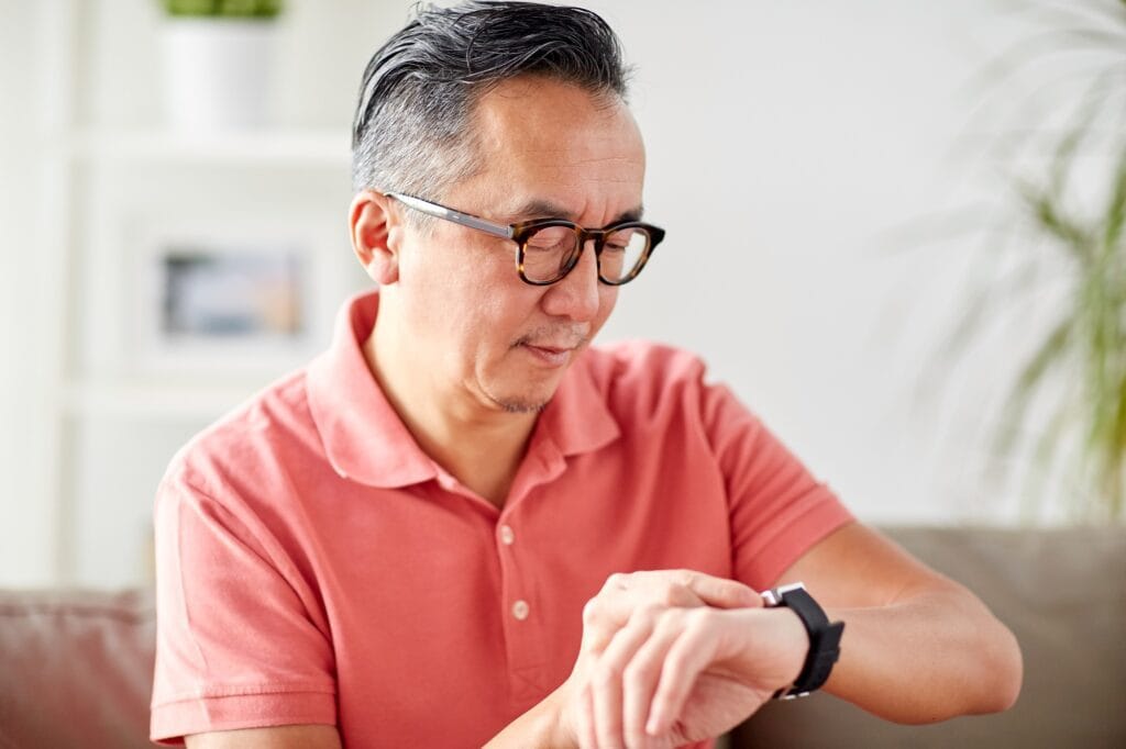 Homem olha as horas. Ele tem cabelos curtos, grisalhos, usa camiseta de botão rosa e está olhando para seu relógio de pulso, como se conferisse os horário Pix.
