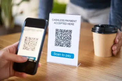 Pessoa usa o celular para escanear QR code em um balcão, demonstrando como receber pelo Pix em vendas presenciais.