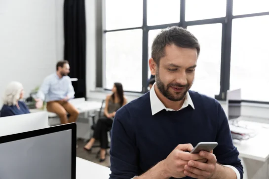 Homem veste uma blusa com manga comprida azul, ele está navegando em seu celular. O homem está procurando como fazer cobrança pelo WhatsApp.