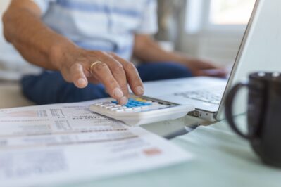 Um empreendedor, está em sua mesa do escritório. Ele está calculando suas cobranças, pesquisando no computador como funciona a antecipação de recebíveis.