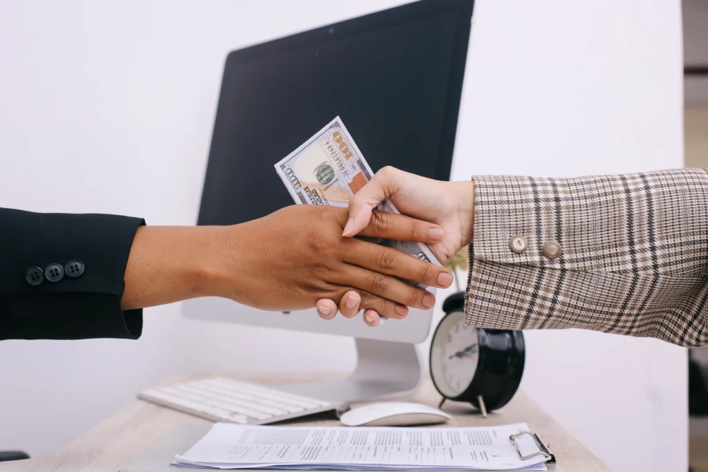 Duas mãos se apertando com notas de dinheiro no meio, representando o processo de como funciona a antecipação de recebíveis.
