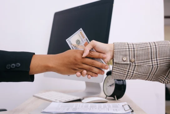 Duas mãos se apertando com notas de dinheiro no meio, representando o processo de como funciona a antecipação de recebíveis.