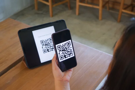 Uma mão está segurando um celular, com a camera apontada para um QR code. Isso representa o Pix agendado.