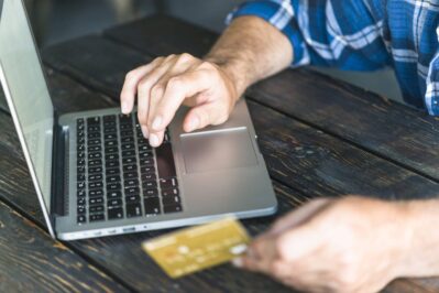 Um empreendedor está no escritório, em frente do notebook, segunrado o carão da empresa. Ele está pesquisando sobre antecipação de recebíveis de cartão de crédito.