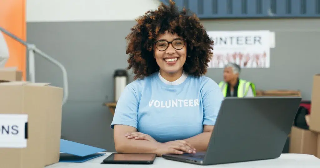 Mulher negra sorrindo, usando laptop em ação voluntária, destacando o uso de aplicativo para receber doações de forma prática.