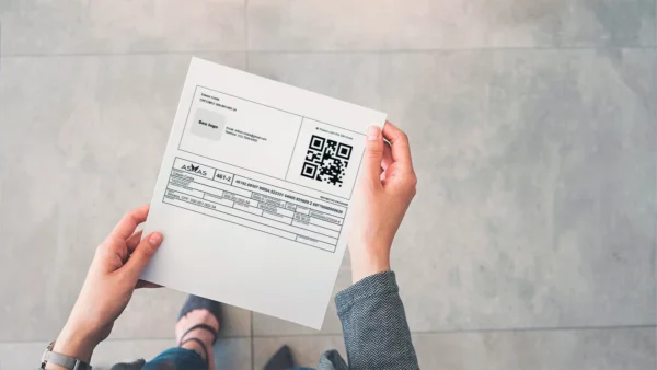 A imagem mostra as mãos de uma mulher segurando um boleto com QR code Pix. Ele foi gerado pelo Asaas.