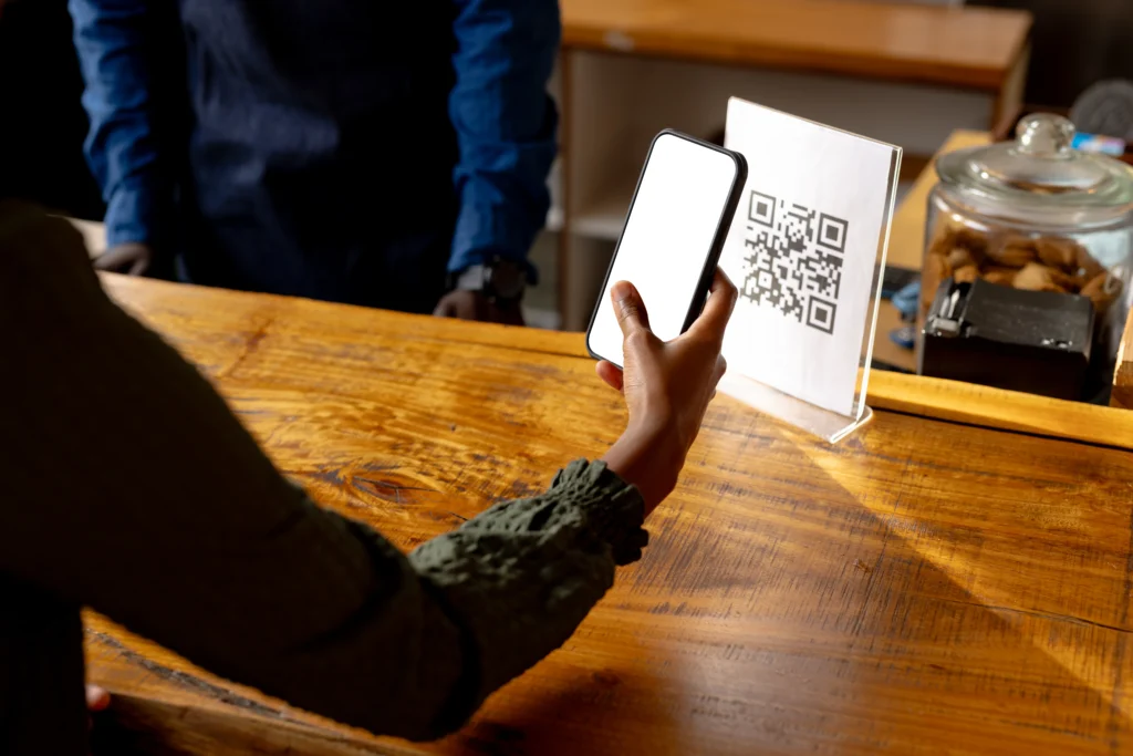 Pessoa escaneia QR code em balcão para pagamento via API Pix, destacando praticidade e rapidez no pagamento instantâneo.