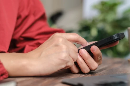 Na imagem, temos um empreended com um celular nas mãos. Ele está buscando como cobrar cliente por mensagem.