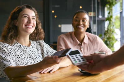 Duas mulheres sorrindo enquanto fazem o pagamento por aproximação no celular, representando a gestão de recebíveis.