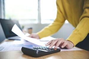 a imagem mostra uma empreendedora em seu escritório, com um computador e uma calculadora sobre a mesa e um recibo na mão. Ela está pesquisando sobre gestão de recebíveis para o seu negócio.